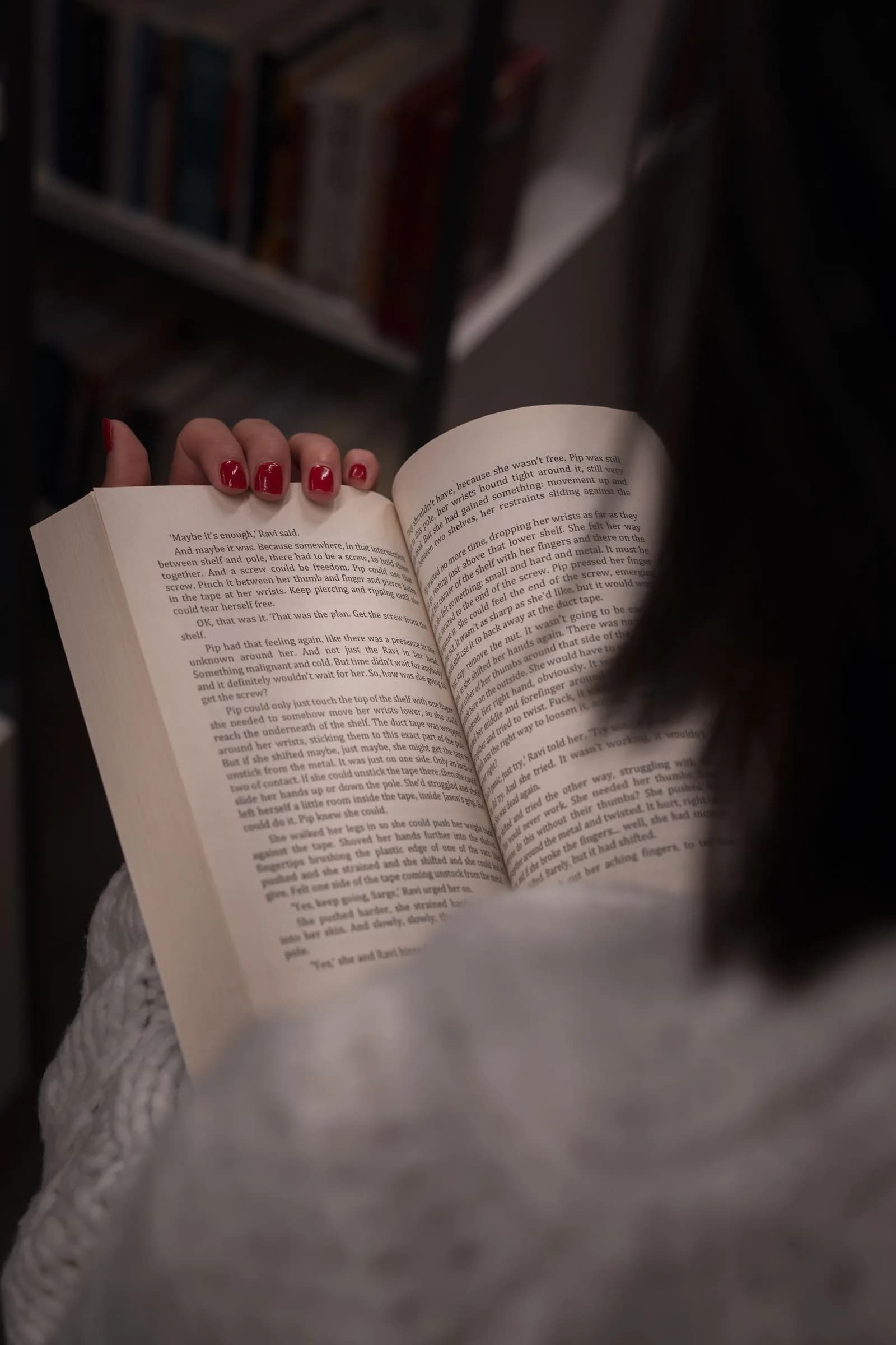 Close-up of a woman's hands holding an open book in a dim home library.