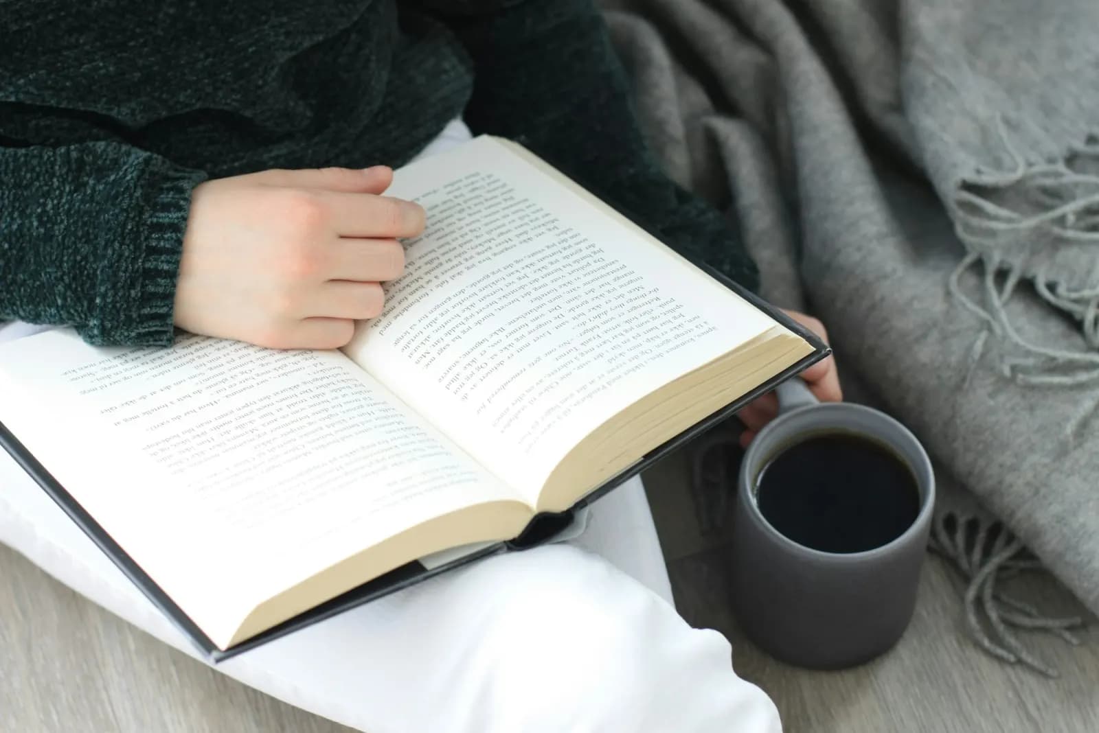 Person sitting with a book and a cup of coffee, reading as part of a daily routine
