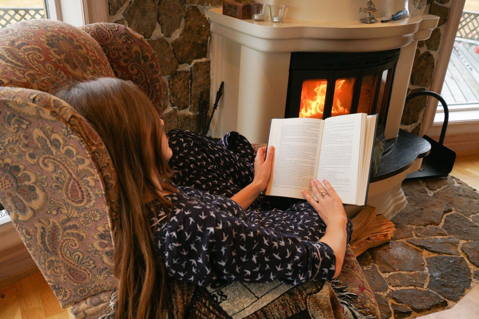 Person reading a book, curled up under a blanket by the fire